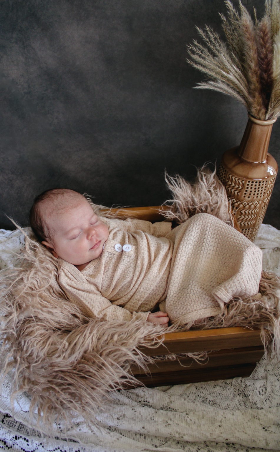 Sleeping newborn wrapped in a blanket in a wooden cradle, photographed by Kaciejeanphotography